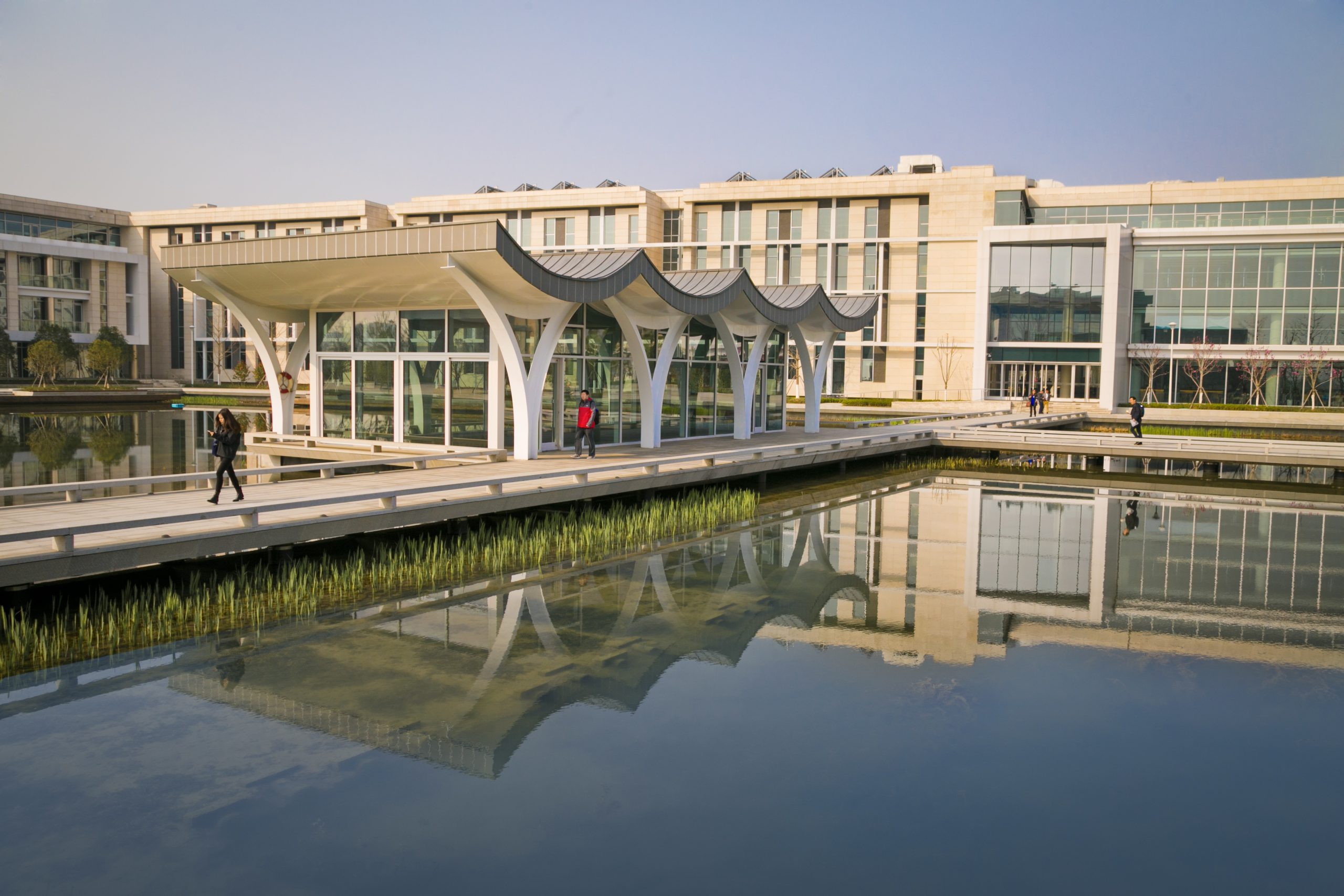 white buildings with curved roofs and many windows surround a large rectangular pond with long walkways