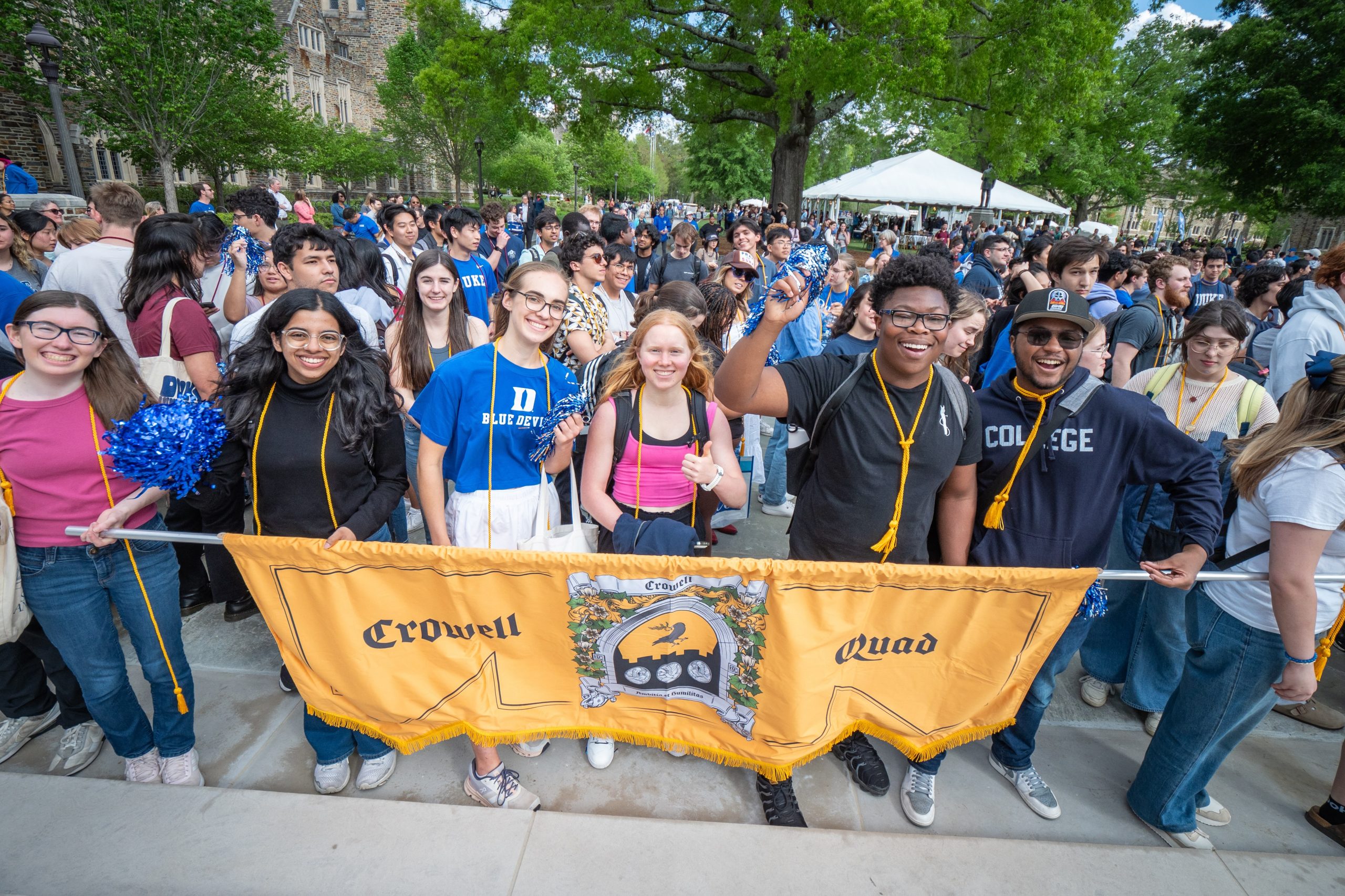 Duke Students walking around the quad holding a yellow Crowell Quad flag.